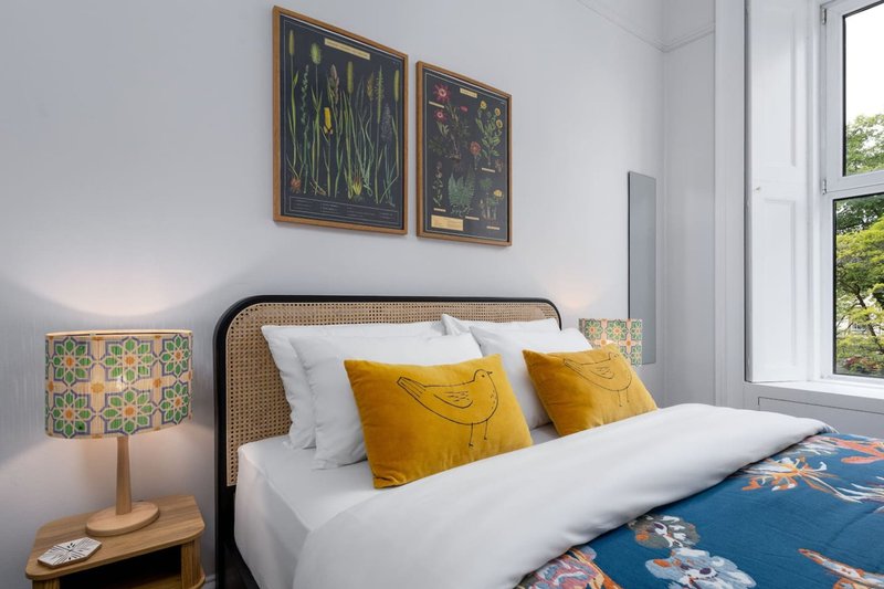 Bright bedroom with rattan headboard, white bedding, mustard cushions and framed artwork