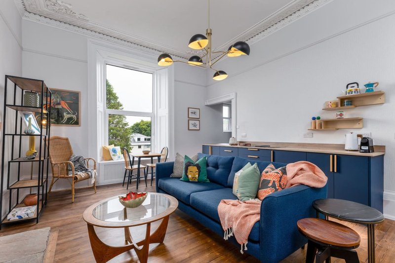 Modern living room with blue sofa, wooden coffee table, shelving, and pendant lighting