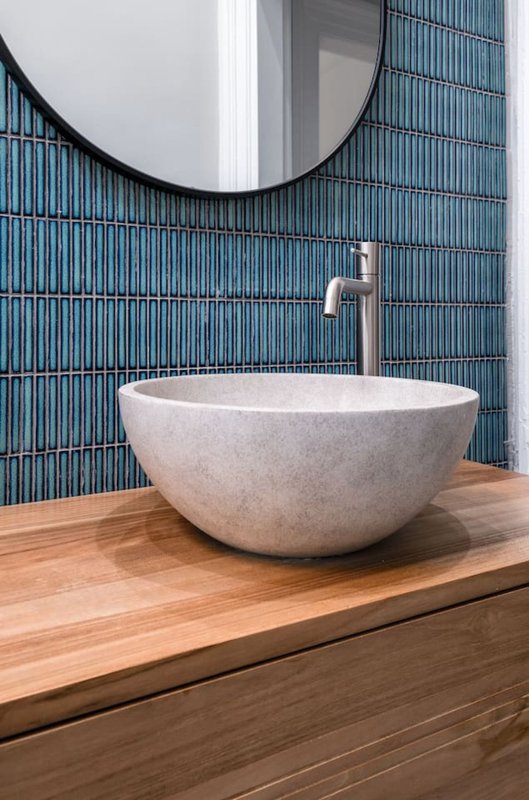 Modern bathroom with round stone basin sink, wooden vanity, blue tile wall and circular mirror