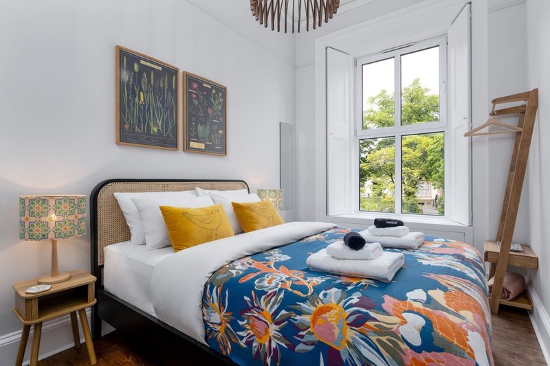 Bright bedroom with double bed, blue patterned duvet, yellow cushions and wooden furniture