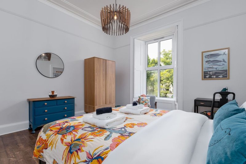 Bright bedroom with double bed, blue dresser, wooden wardrobe and round mirror