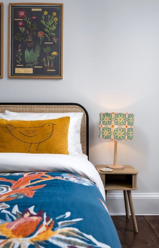 Bedroom with double bed, yellow pillow, blue patterned duvet, wooden nightstand and lamp