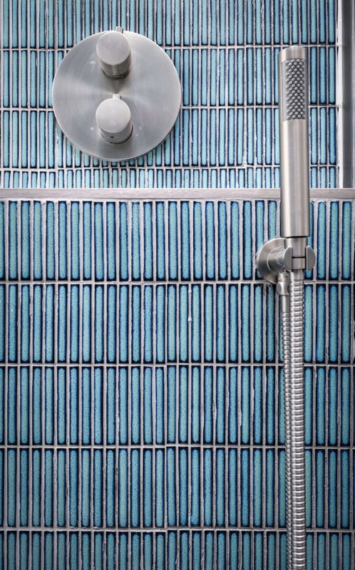 Modern shower head and valve mounted on blue ribbed bathroom wall tile