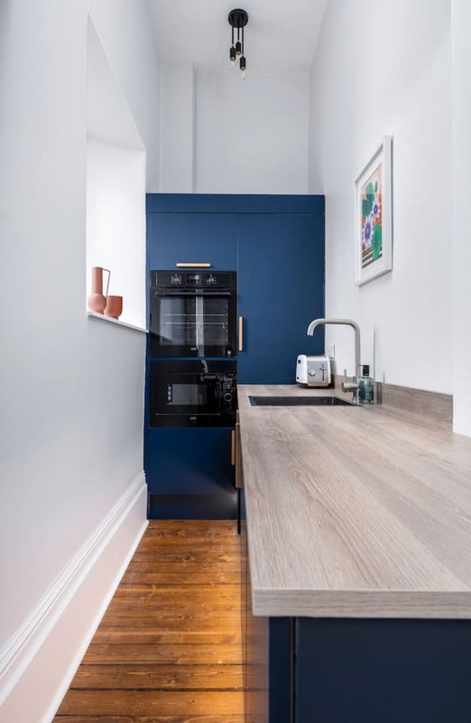 Modern galley kitchen with dark blue cabinetry, grey countertop, black appliances and white walls