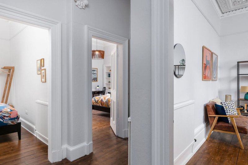 Modern hallway with white walls, wooden flooring, and open doorways leading to bedroom and living areas