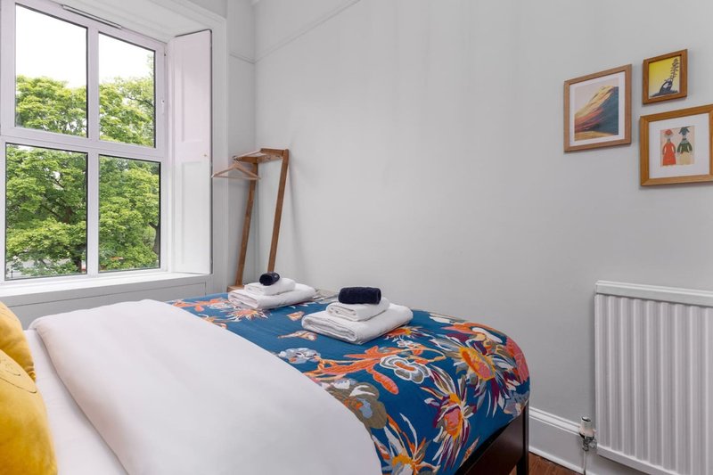 Bright bedroom with double bed, colorful throw, framed wall art and large window with garden view