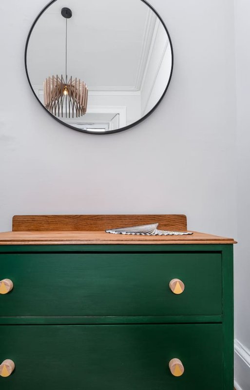 Green wooden dresser with wooden top, round mirror above, and pendant lamp reflected