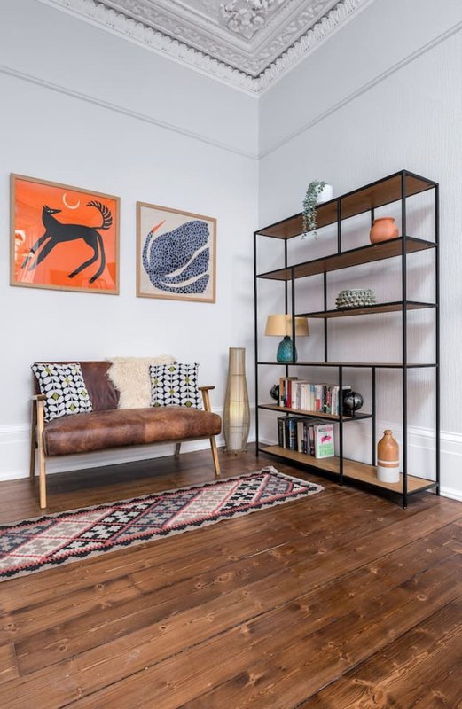 Living room with brown leather sofa, geometric wall art, black shelving unit, patterned rug and wooden floors