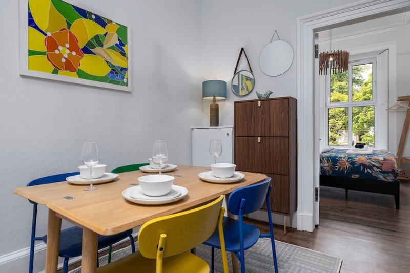 Dining room with wooden table, blue and yellow chairs, white tableware, and colorful wall art