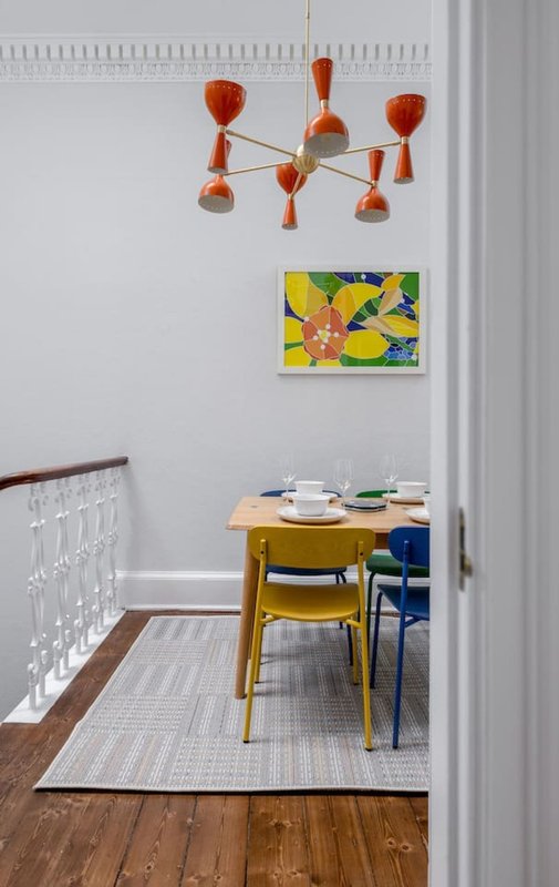 Dining area with wooden table, colorful chairs, pendant lamp and framed artwork on wall