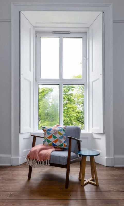 Bright interior window seat with mid-century chair, colorful cushion, and garden view