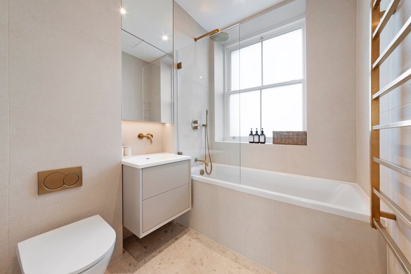Modern bathroom with white vanity, bathtub, toilet, and large window with natural light