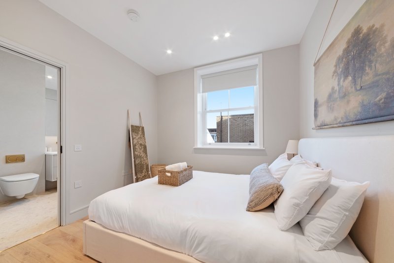 Modern bedroom with double bed, white bedding, wooden floor and ensuite bathroom visible
