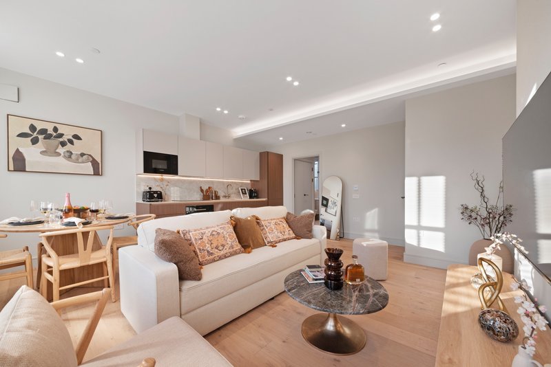 Modern open-plan living room with cream sofa, wooden dining table, and kitchen area with neutral tones