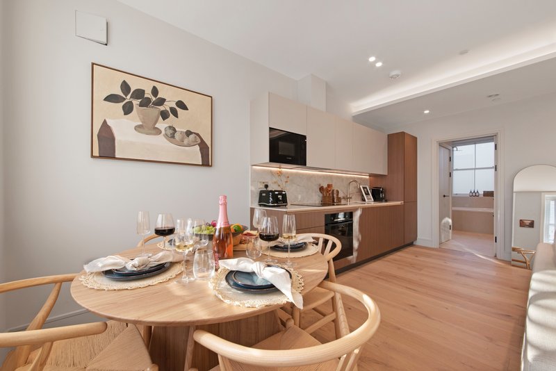 Modern open-plan kitchen and dining area with round wooden table, place settings, and wine bottles