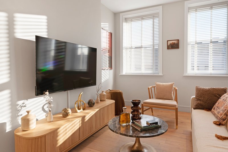 Bright living room with wall-mounted TV, wooden media console, armchair, and round glass coffee table
