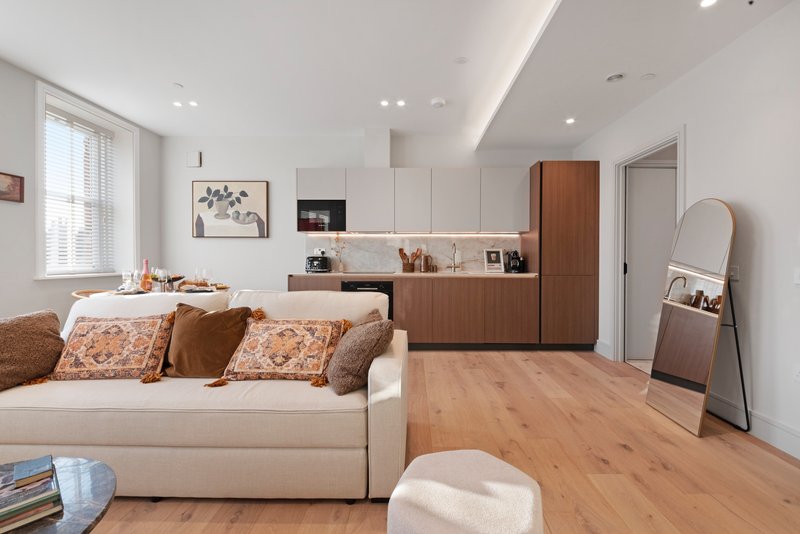 Modern open-plan living room with cream sofa, wooden cabinetry, and light wood flooring