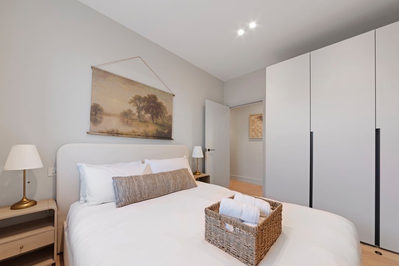 Modern bedroom with white bed, wooden nightstands, wall art, and built-in wardrobes