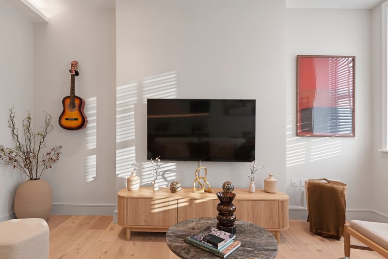 Modern living room with wall-mounted TV, wooden media console, acoustic guitar wall decoration, and abstract wall art