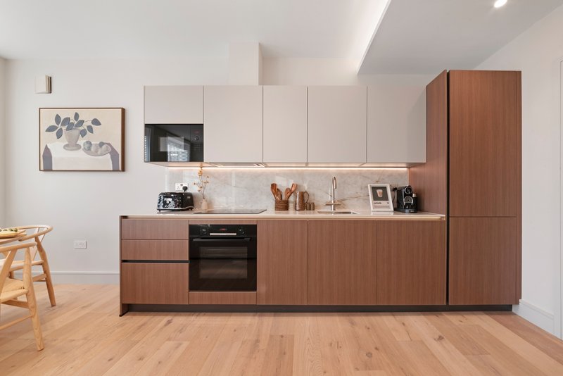 Modern kitchen with wooden cabinetry, built-in oven, white countertop, and wooden flooring