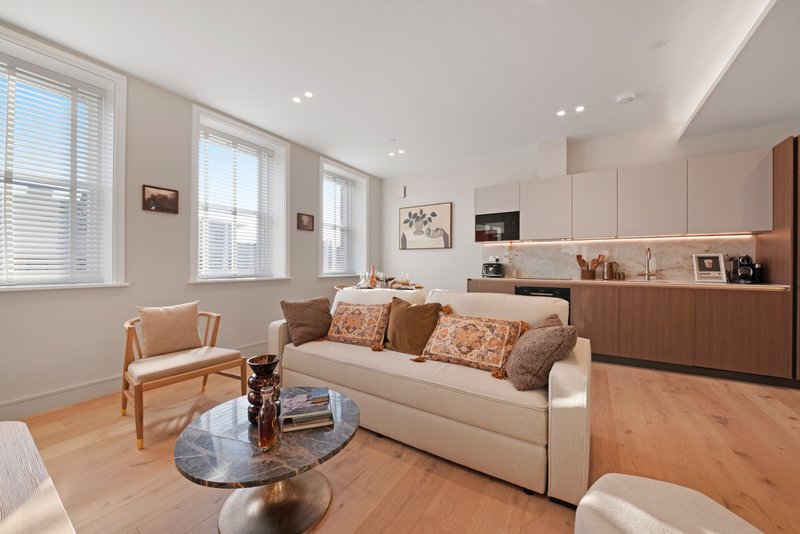 Modern open-plan living room and kitchen with cream sofa, wooden chair, and hardwood flooring