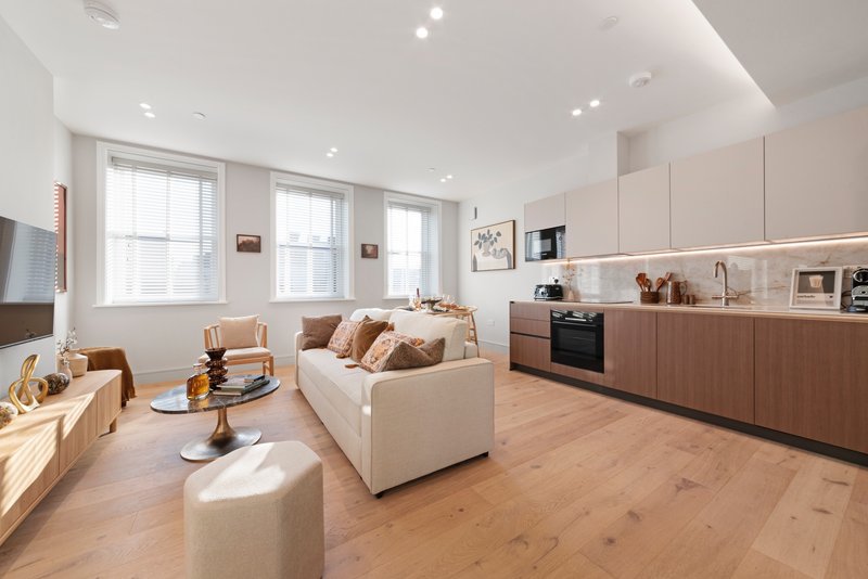 Open-plan living and kitchen area with cream sofa, wooden flooring, and modern cabinetry