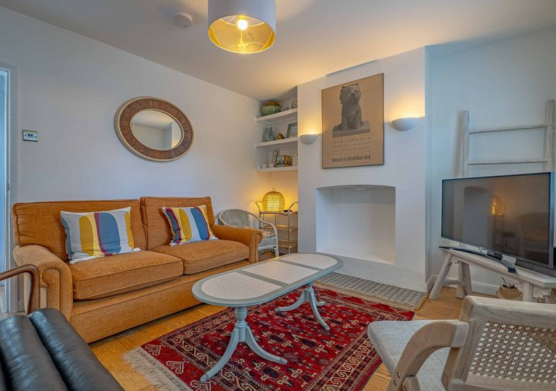 Living room with tan sofa, red rug, fireplace, wall shelving and television