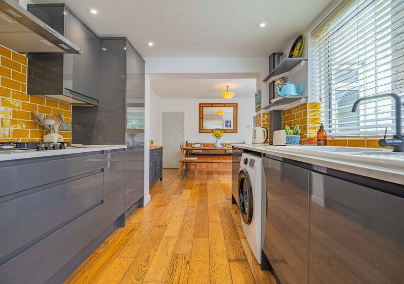 Modern kitchen with grey cabinetry, yellow tile backsplash, wooden floor and integrated washing machine