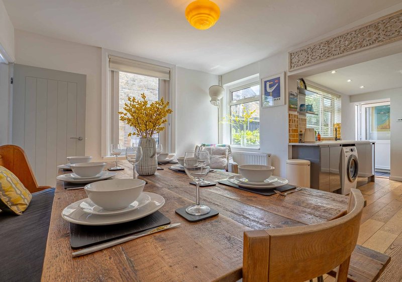 Open-plan dining and kitchen area with wooden table, place settings, and yellow flowers