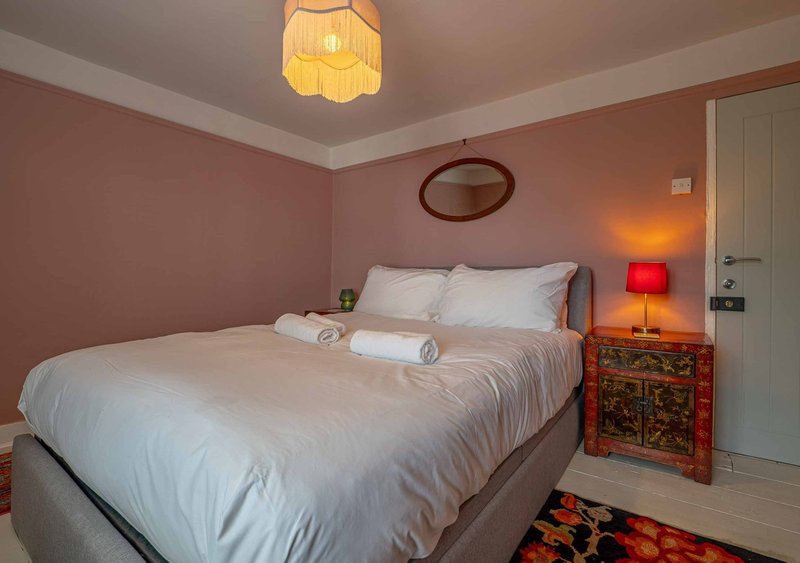 Bedroom with double bed, pink walls, bedside table, lamp and ceiling light fixture