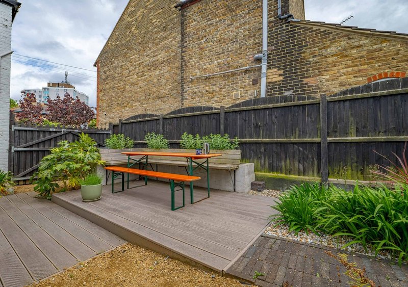 Outdoor patio with picnic table, wooden decking, plants, and brick building backdrop