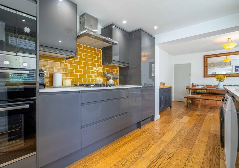 Modern kitchen with gray cabinetry, yellow brick backsplash, wooden flooring and stainless steel appliances