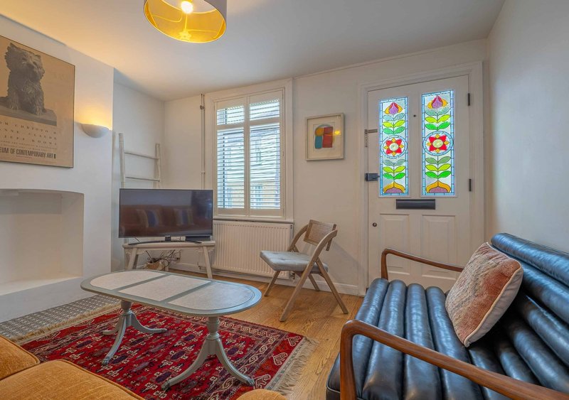Bright living room with sofa, wooden chairs, glass coffee table, television and stained glass window panels