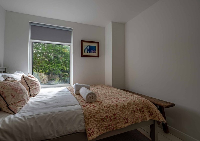 Bright bedroom with single bed, patterned bedding, window overlooking garden and framed artwork