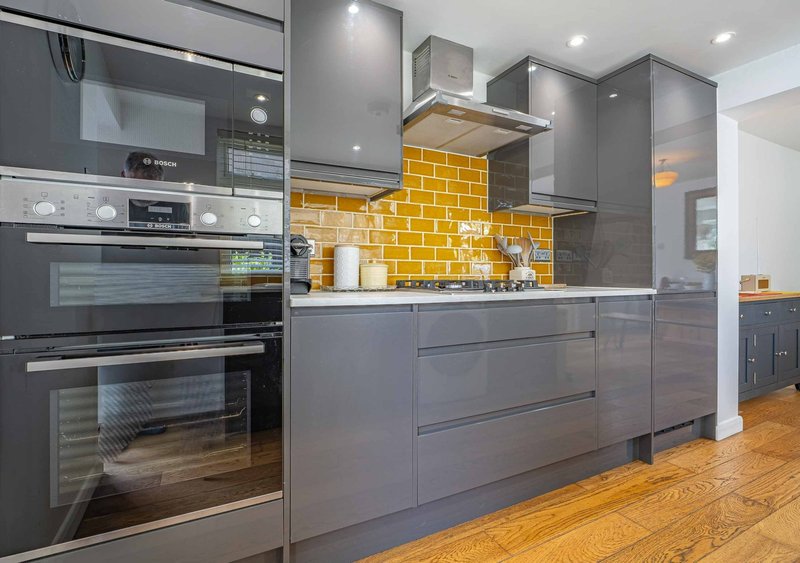 Modern kitchen with grey cabinetry, yellow tile backsplash, stainless steel appliances and wooden flooring