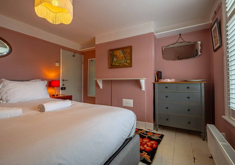 Pink bedroom with double bed, dresser, ceiling lamp and en-suite bathroom door