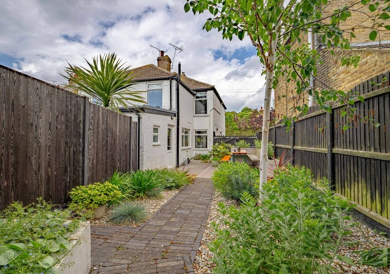 Rear garden pathway with brick paving, fenced sides, and white two-storey house