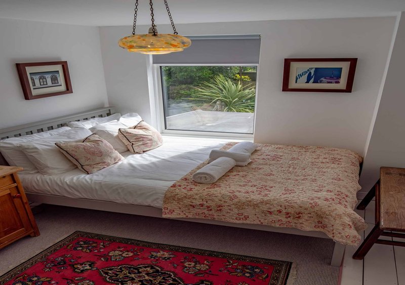 Bright bedroom with two beds, pendant lamp, framed artwork, and garden view through sliding door
