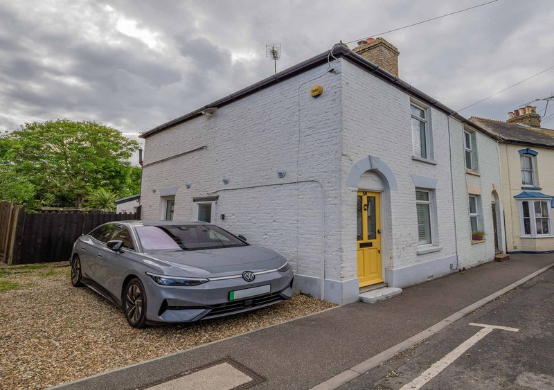 White rendered semi-detached house with yellow door, driveway, and parked car