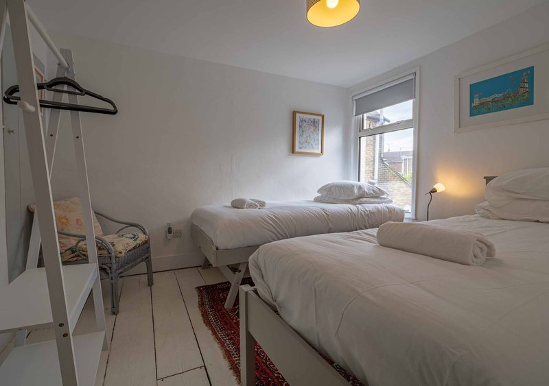 Bright bedroom with two white beds, wooden floor, ladder shelving, and window with sea view