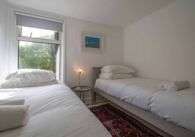 Bright bedroom with two single beds, white bedding, window with views, and small side table