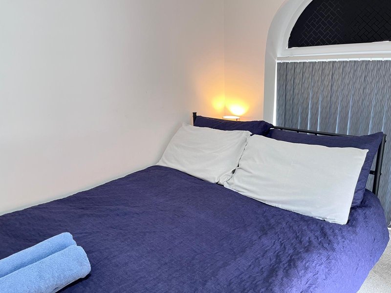 Bedroom with double bed, white pillows, dark blue bedding, arched window and wall light