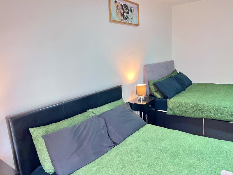 Bedroom with two single beds, green bedding, black headboards, small lamp, and framed wall art