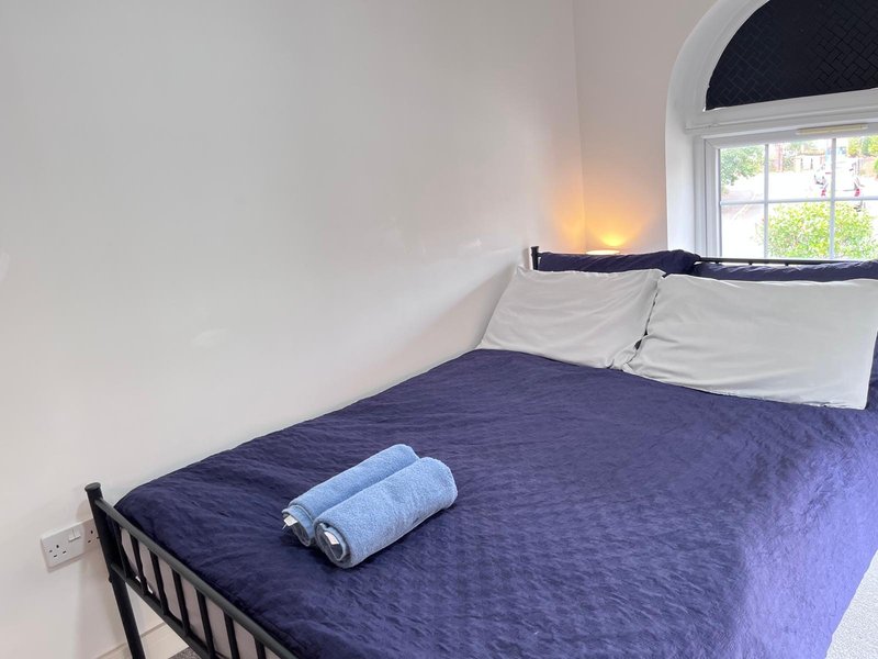 Bedroom with single bed, navy bedding, white pillows, rolled towels, and arched window