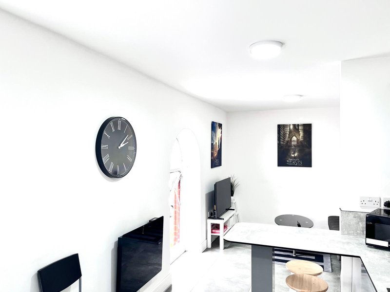 Modern kitchen with white walls, dark clock, desk area, microwave and dining setup