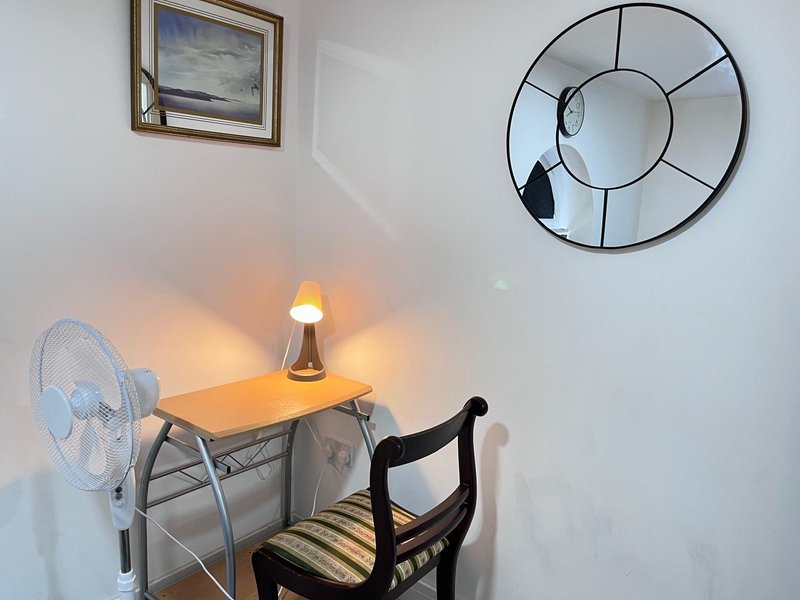 Small bedroom corner with desk, chair, lamp, fan, and wall mirrors