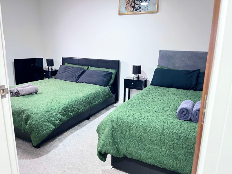 Bedroom with two beds with green quilts, black headboards, bedside tables and lamps