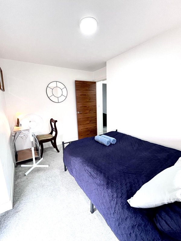 Bright bedroom with double bed, desk chair, wooden wardrobe, and wall clock