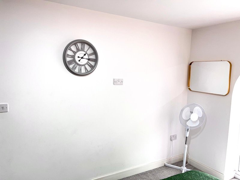 Minimalist room corner with wall clock, mirror, white fan and light switch
