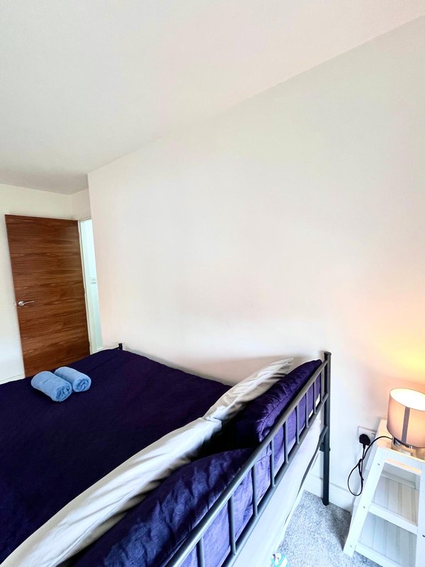Compact bedroom with single bed, dark blue bedding, wooden door and bedside lamp
